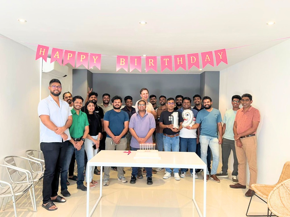 Zeropoint's 19th birthday celebration: the team gathered around a cake under a Happy Birthday banner